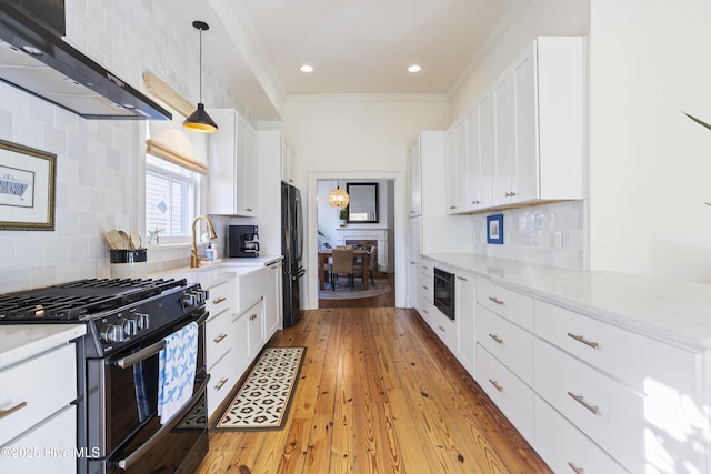 kitchen with white cabinets, wall chimney range hood, freestanding refrigerator, range with gas cooktop, and crown molding