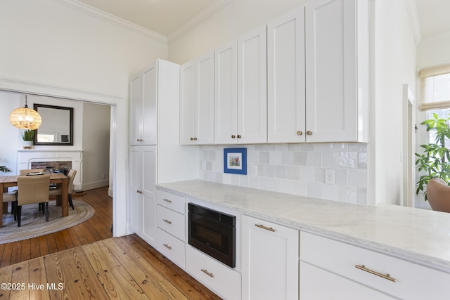 kitchen with white cabinets, black microwave, decorative backsplash, and ornamental molding