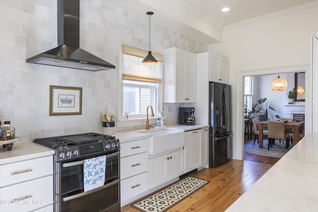 kitchen featuring sink, black refrigerator with ice dispenser, pendant lighting, range with two ovens, and wall chimney range hood