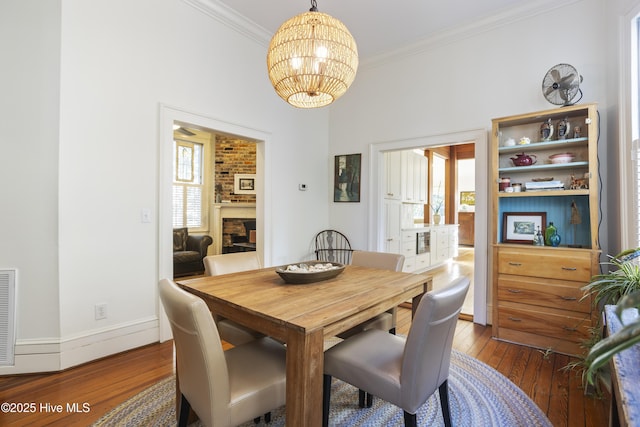 dining space featuring hardwood / wood-style flooring, a notable chandelier, baseboards, a brick fireplace, and crown molding