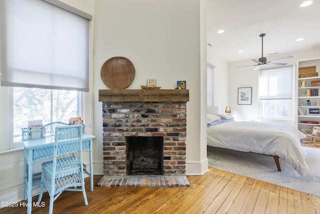 bedroom with multiple windows, a fireplace, light hardwood / wood-style flooring, and ceiling fan