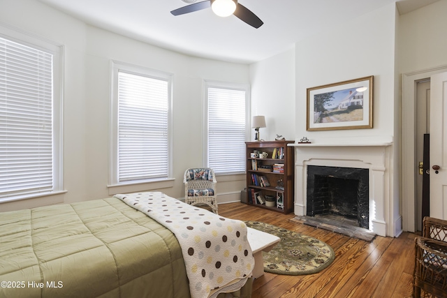 bedroom with ceiling fan, a high end fireplace, and hardwood / wood-style floors