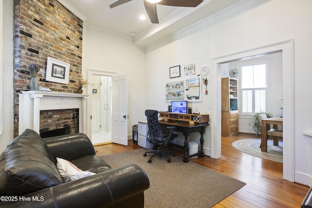 home office featuring hardwood / wood-style flooring, a fireplace, a ceiling fan, baseboards, and ornamental molding