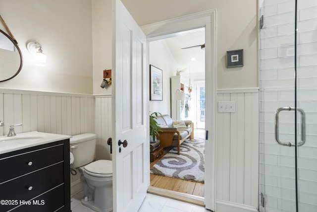 ensuite bathroom featuring toilet, a shower stall, vanity, and wainscoting