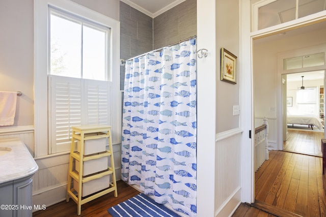 bathroom featuring a shower with shower curtain, wainscoting, wood-type flooring, ornamental molding, and vanity