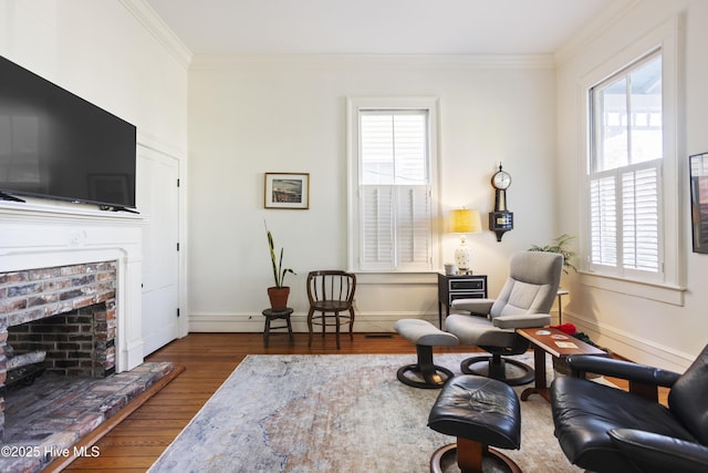 living area featuring a brick fireplace, crown molding, baseboards, and wood finished floors