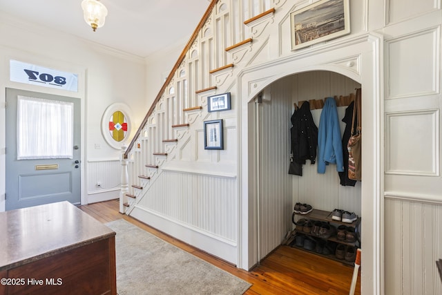 foyer with a wainscoted wall, crown molding, stairway, and light wood finished floors