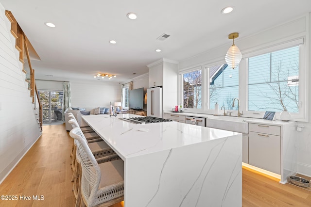 kitchen with light stone counters, white cabinets, decorative light fixtures, a breakfast bar, and a spacious island