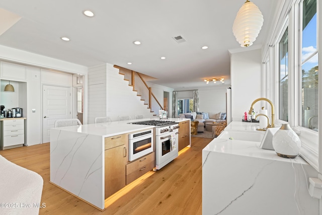 kitchen with light wood-type flooring, built in microwave, light stone countertops, sink, and high end stove