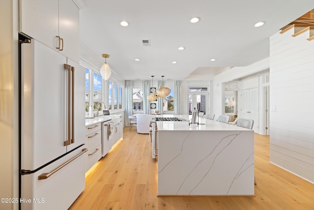 kitchen with light hardwood / wood-style flooring, high end fridge, an island with sink, pendant lighting, and white cabinetry