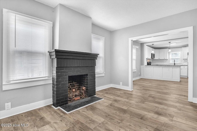 unfurnished living room with a fireplace, sink, a textured ceiling, and light wood-type flooring