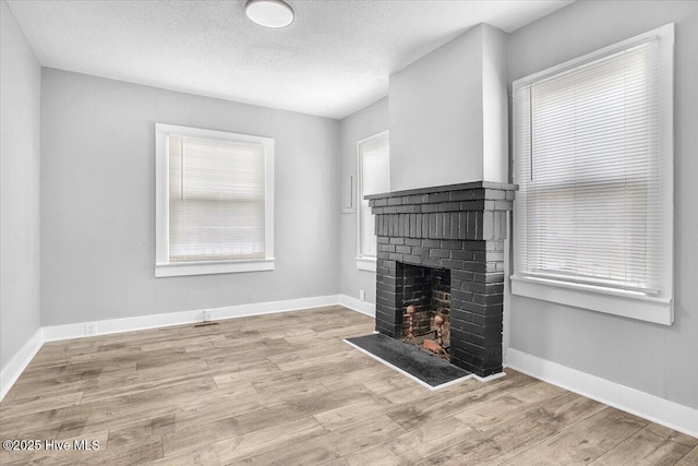 unfurnished living room featuring a brick fireplace, light hardwood / wood-style flooring, and a textured ceiling