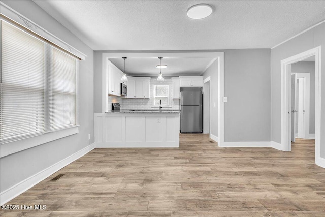 kitchen featuring stainless steel appliances, tasteful backsplash, light stone countertops, white cabinets, and decorative light fixtures