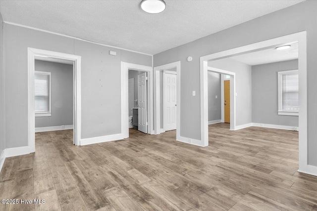 unfurnished bedroom featuring multiple windows, light hardwood / wood-style floors, and a textured ceiling