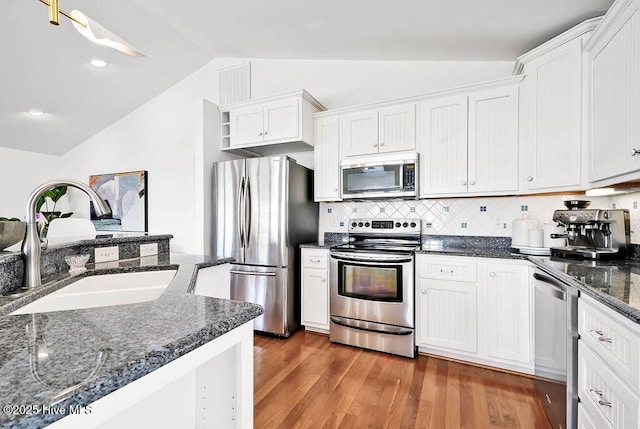 kitchen with a sink, wood finished floors, white cabinetry, appliances with stainless steel finishes, and lofted ceiling