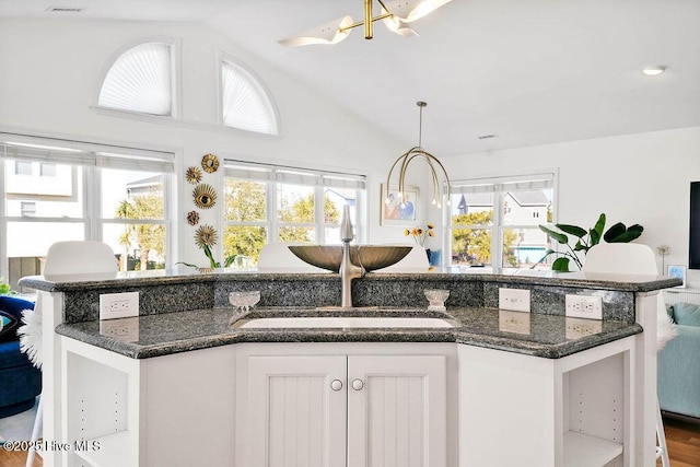 kitchen with a sink, dark stone countertops, an inviting chandelier, white cabinets, and lofted ceiling