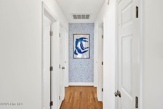 hallway with wallpapered walls, light wood-style floors, visible vents, and baseboards