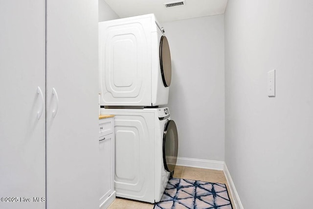 clothes washing area featuring visible vents, cabinet space, stacked washer and clothes dryer, and baseboards