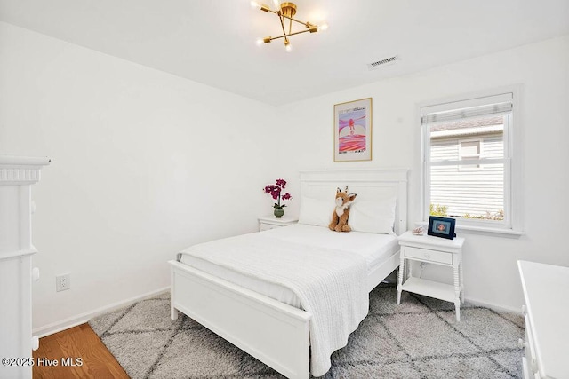 bedroom with a notable chandelier, wood finished floors, visible vents, and baseboards