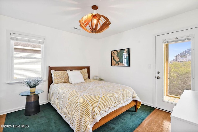 bedroom featuring visible vents, wood finished floors, baseboards, and access to outside