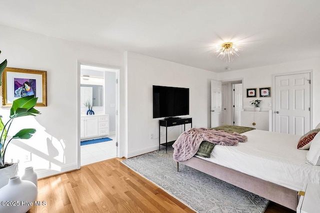 bedroom with connected bathroom, baseboards, and light wood finished floors