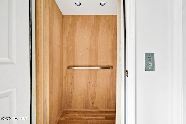 details with elevator, wooden walls, and wood finished floors