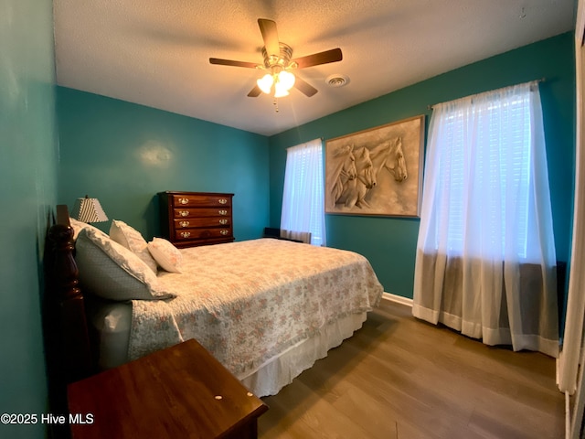 bedroom with hardwood / wood-style flooring, ceiling fan, multiple windows, and a textured ceiling