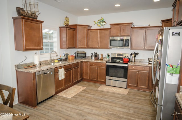 kitchen with appliances with stainless steel finishes, light hardwood / wood-style floors, sink, and light stone countertops