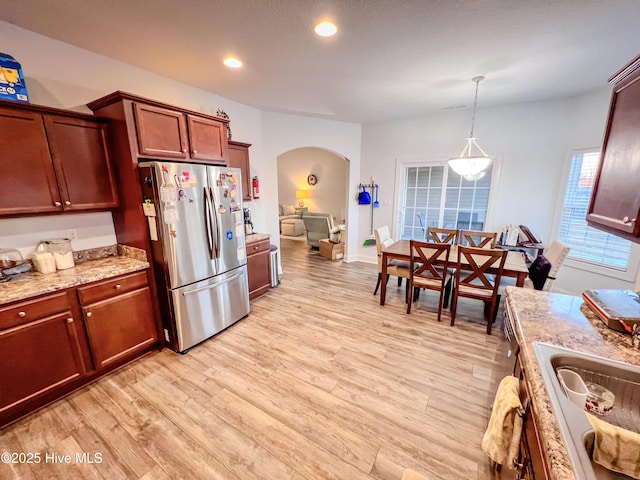 kitchen with light stone counters, stainless steel fridge, hanging light fixtures, and light hardwood / wood-style flooring