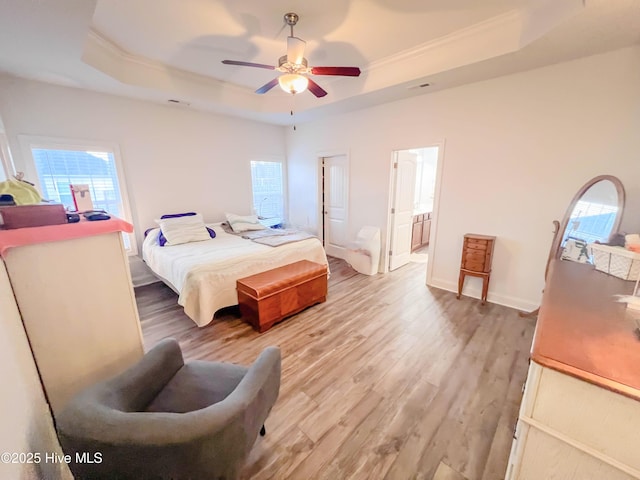 bedroom with hardwood / wood-style flooring, ceiling fan, a tray ceiling, crown molding, and ensuite bath