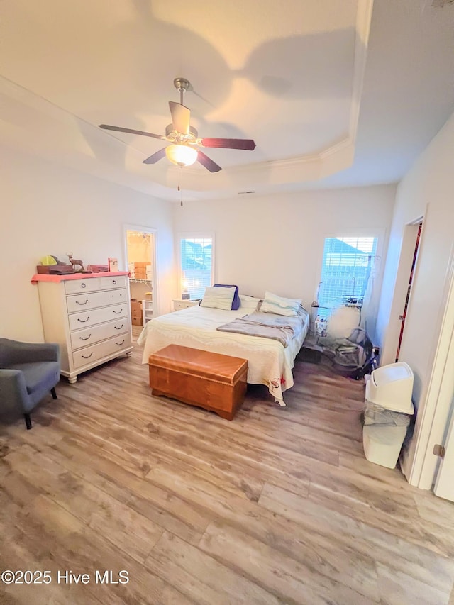 bedroom featuring a raised ceiling, ensuite bath, ceiling fan, and light hardwood / wood-style floors