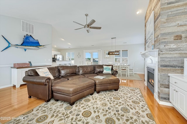 living room featuring lofted ceiling, a large fireplace, ceiling fan, and light wood-type flooring