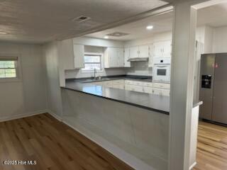 kitchen featuring plenty of natural light, white cabinets, stainless steel fridge with ice dispenser, white oven, and light wood-type flooring