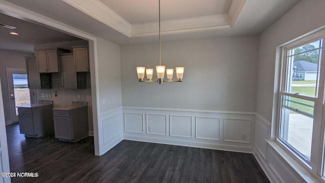 unfurnished dining area featuring a raised ceiling, dark wood-type flooring, and an inviting chandelier