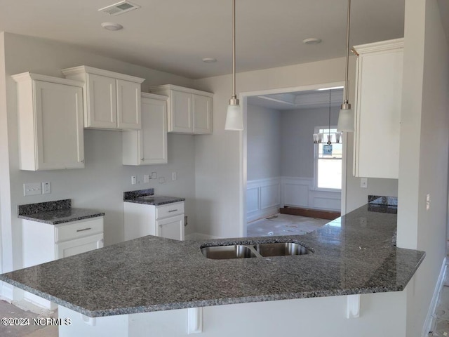 kitchen featuring white cabinetry, dark stone counters, kitchen peninsula, and hanging light fixtures