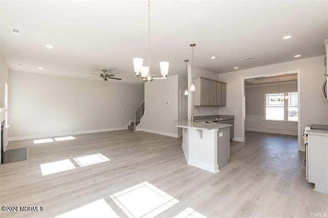 kitchen featuring hanging light fixtures, ceiling fan with notable chandelier, a kitchen bar, and light hardwood / wood-style floors