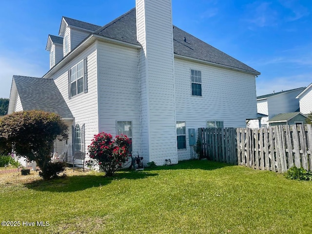 rear view of property featuring fence, a lawn, a shingled roof, and a chimney
