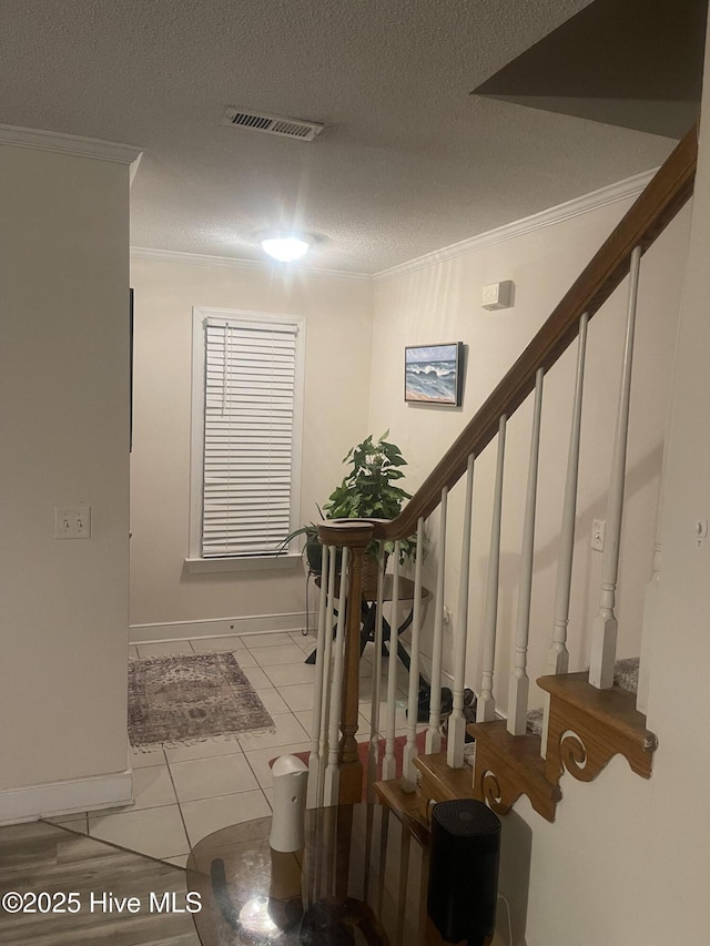 interior space with a textured ceiling, baseboards, visible vents, stairs, and crown molding