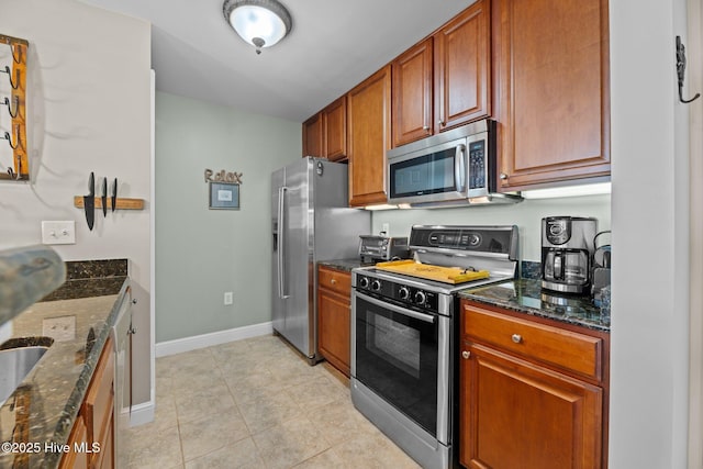 kitchen featuring light tile patterned flooring, appliances with stainless steel finishes, and dark stone countertops