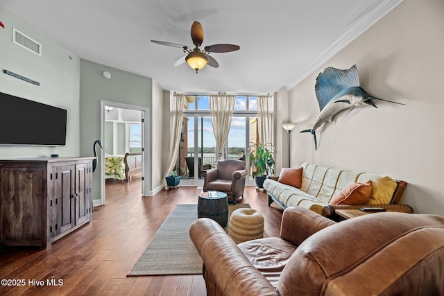 living room featuring dark wood-type flooring, ornamental molding, and ceiling fan