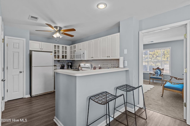 kitchen with white appliances, a breakfast bar, white cabinets, decorative backsplash, and kitchen peninsula