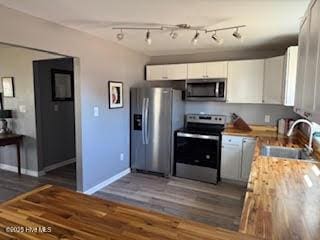 kitchen with appliances with stainless steel finishes, dark hardwood / wood-style floors, white cabinetry, sink, and wooden counters