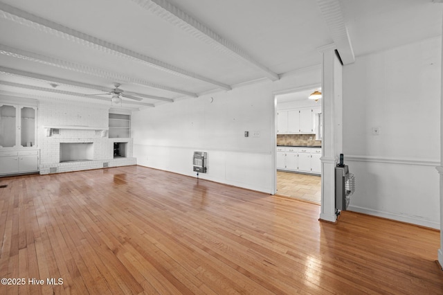 unfurnished living room featuring heating unit, a fireplace, beamed ceiling, ceiling fan, and light hardwood / wood-style floors