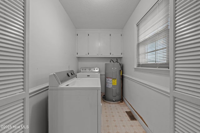 clothes washing area featuring water heater, washer and clothes dryer, a textured ceiling, and cabinets