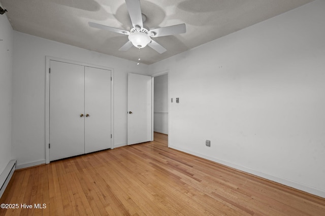 unfurnished bedroom featuring ceiling fan, a baseboard heating unit, light wood-type flooring, and a closet