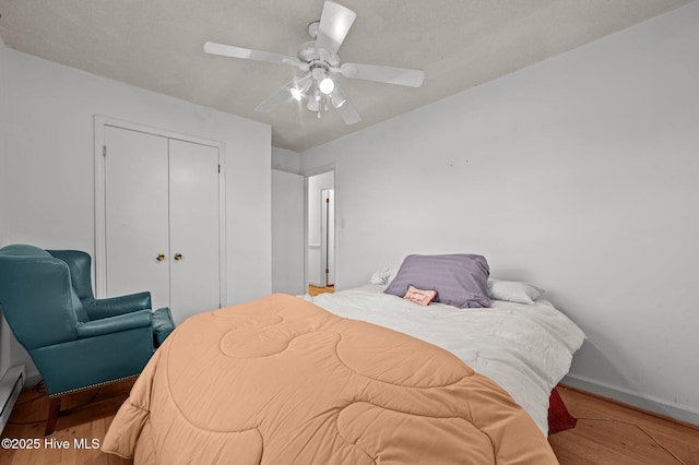 bedroom featuring hardwood / wood-style flooring, ceiling fan, a closet, and a baseboard heating unit