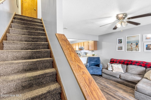 stairway with ceiling fan, wood-type flooring, and a textured ceiling