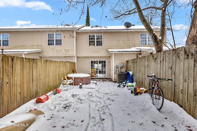 snow covered back of property featuring central AC unit and a hot tub