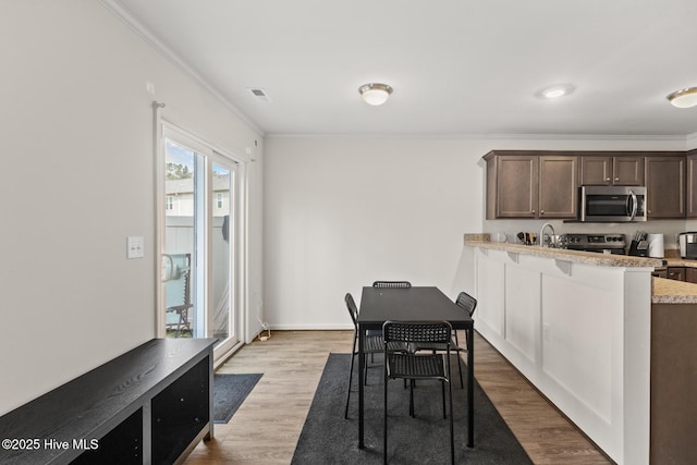 kitchen featuring dark brown cabinetry, crown molding, light stone counters, light hardwood / wood-style flooring, and stainless steel appliances