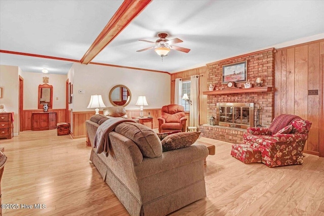 living room featuring wood walls, a brick fireplace, light wood-type flooring, ornamental molding, and ceiling fan